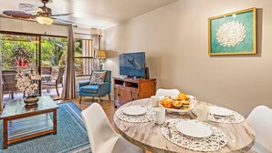 A dining area with a round marble table, white chairs, and a television on a wooden cabinet. - Where Aloha Welcomes You Kihei Condo Private Lanai Pool Steps to the Beach (Kihei)