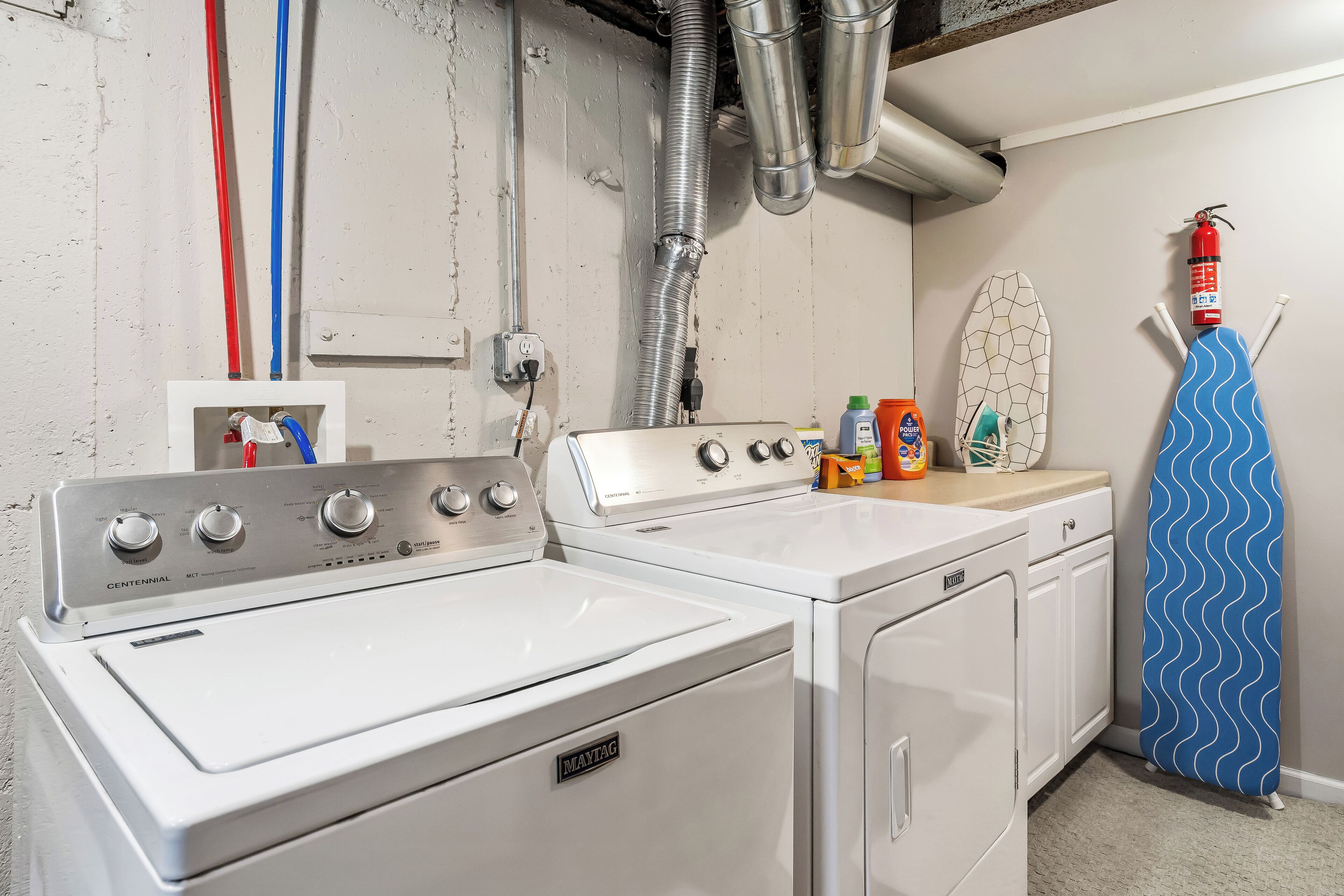 A laundry room with a Maytag washer and dryer, a fire extinguisher, and a surfboard.