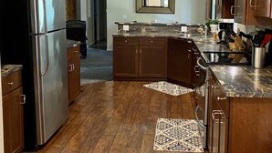Une cuisine dotée de meubles en bois, d’un réfrigérateur en acier inoxydable, d’un ventilateur de plafond et d’un plan de travail en marbre.