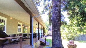 Une véranda abritée avec des sièges d’extérieur, un grand arbre et un foyer.
