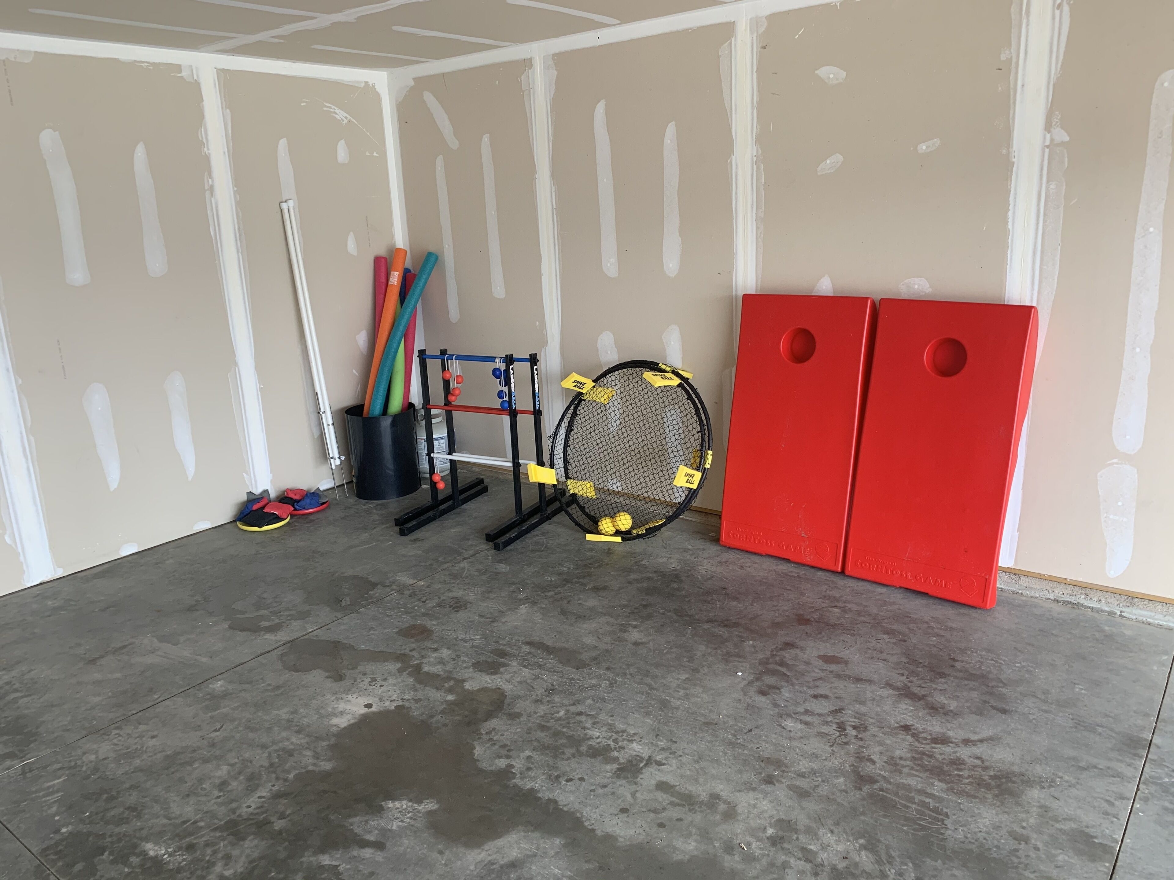 A room with a concrete floor, white walls with visible studs, a badminton net, and two red cabinets.