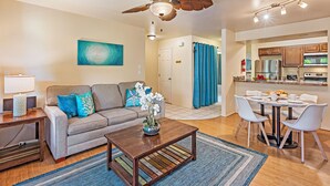 A modern living room with a ceiling fan, a dining area with a table and chairs, and a kitchen visible through an open door. - Where Serenity Awaits Kihei Spacious Condo Private Lanai Pool Near Beach (Kihei)
