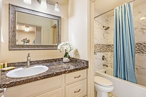 A bathroom with a marble sink, a white toilet, a shower with a blue curtain, and a mirror with lights. - Where Serenity Awaits Kihei Spacious Condo Private Lanai Pool Near Beach (Kihei)