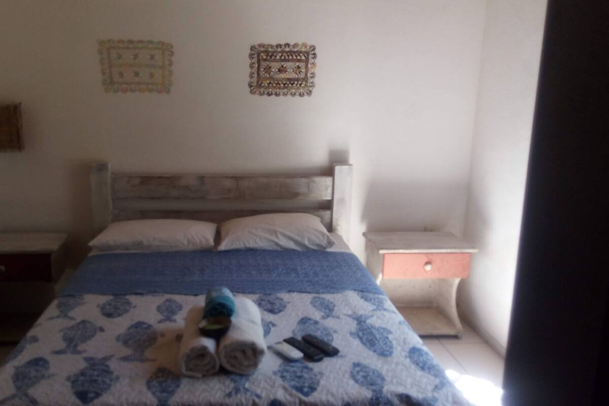 Un dormitorio con cama, dos mesitas de noche, cómoda y dos adornos en la pared.
