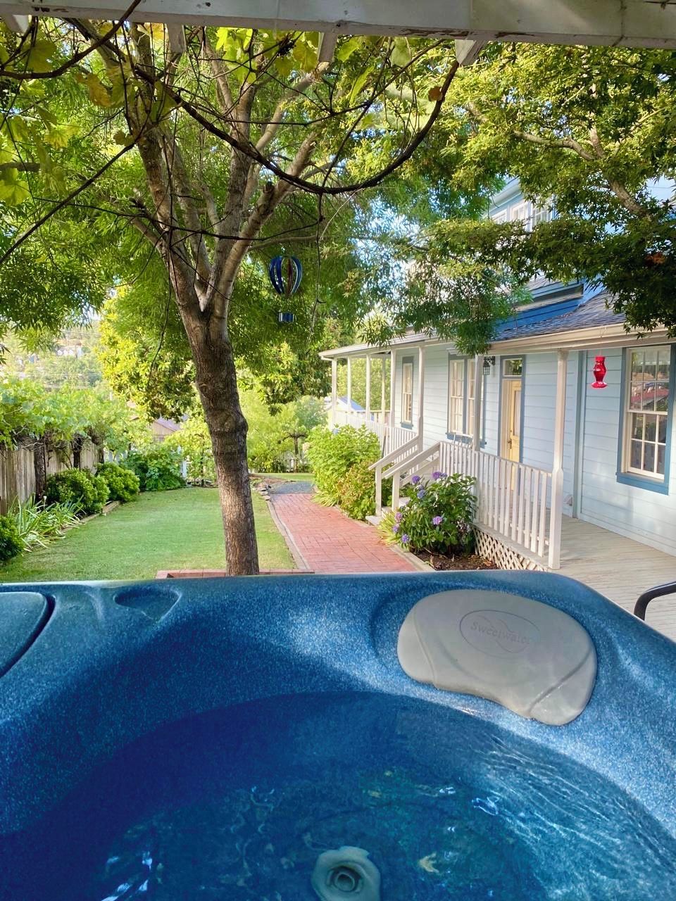 A hot tub in a backyard with a tree, a house, and a brick pathway.