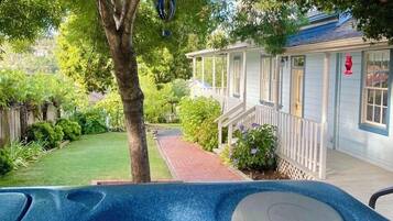A hot tub in a backyard with a tree, a house, and a brick pathway.