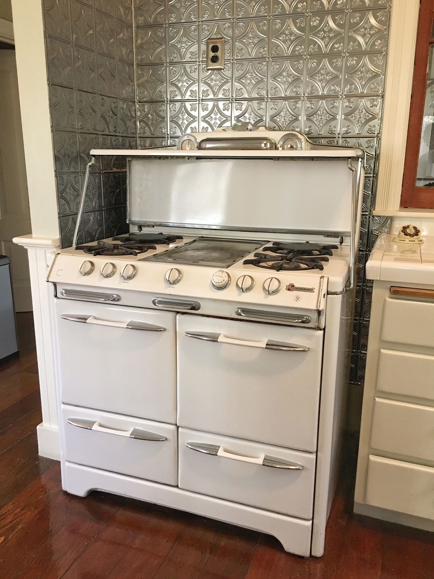 Een witte fornuis met vier branders, een afzuigkap en een dubbele oven.
