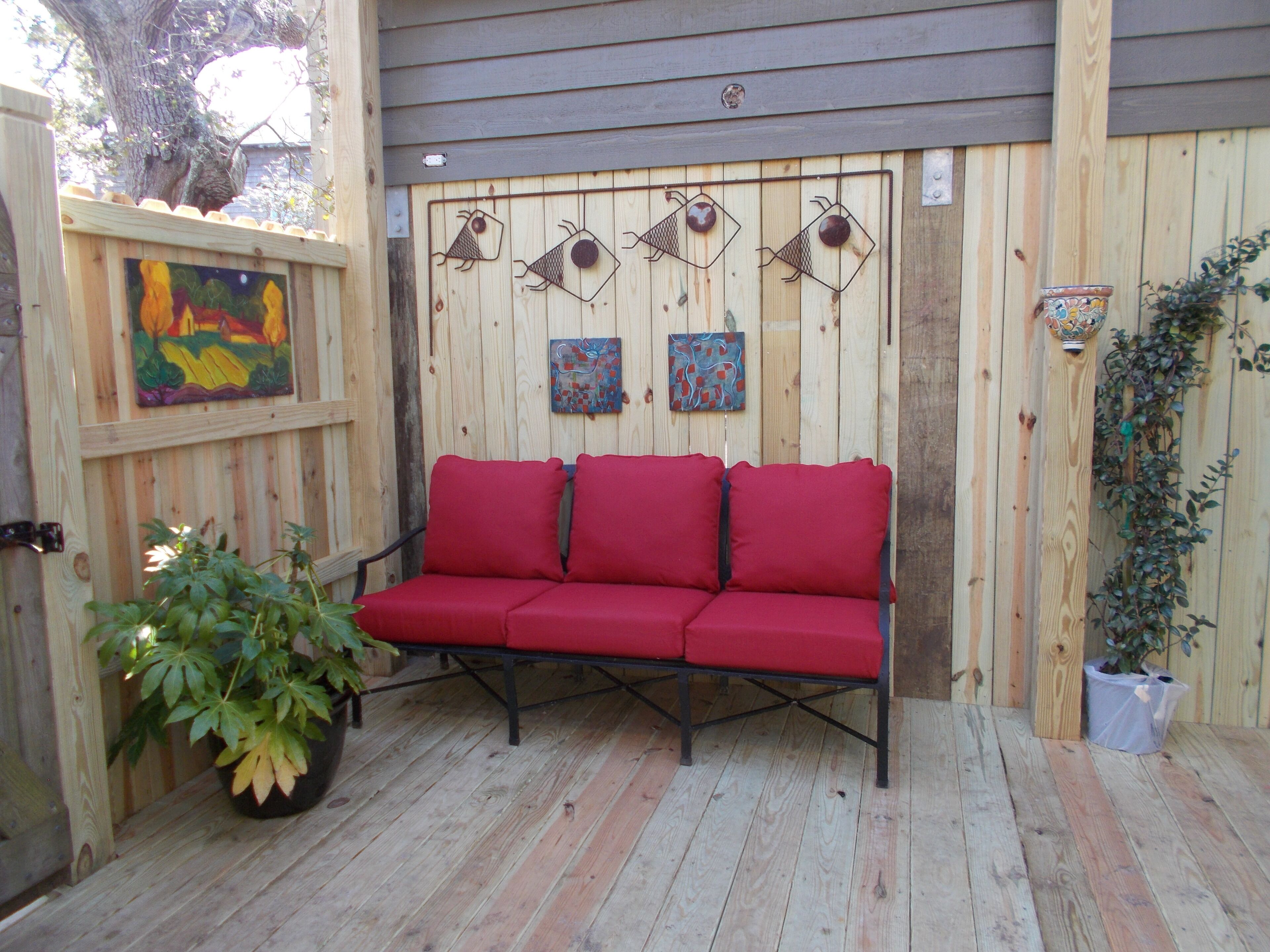 A wooden deck with a red sofa, two paintings, and a potted plant.