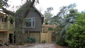 Una casa de dos pisos con terraza de madera y patio trasero cercado.