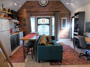 A cozy kitchen with a wooden ceiling, a dining table with a colorful runner, a teal sofa, and a red patterned rug. - Beautiful, Historic and Private Retreat for Couples-limit 2 people (Ocracoke)