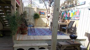 Una terraza de madera con un tapete azul estampado, una parrilla para barbacoa y una mesa de comedor con sillas.