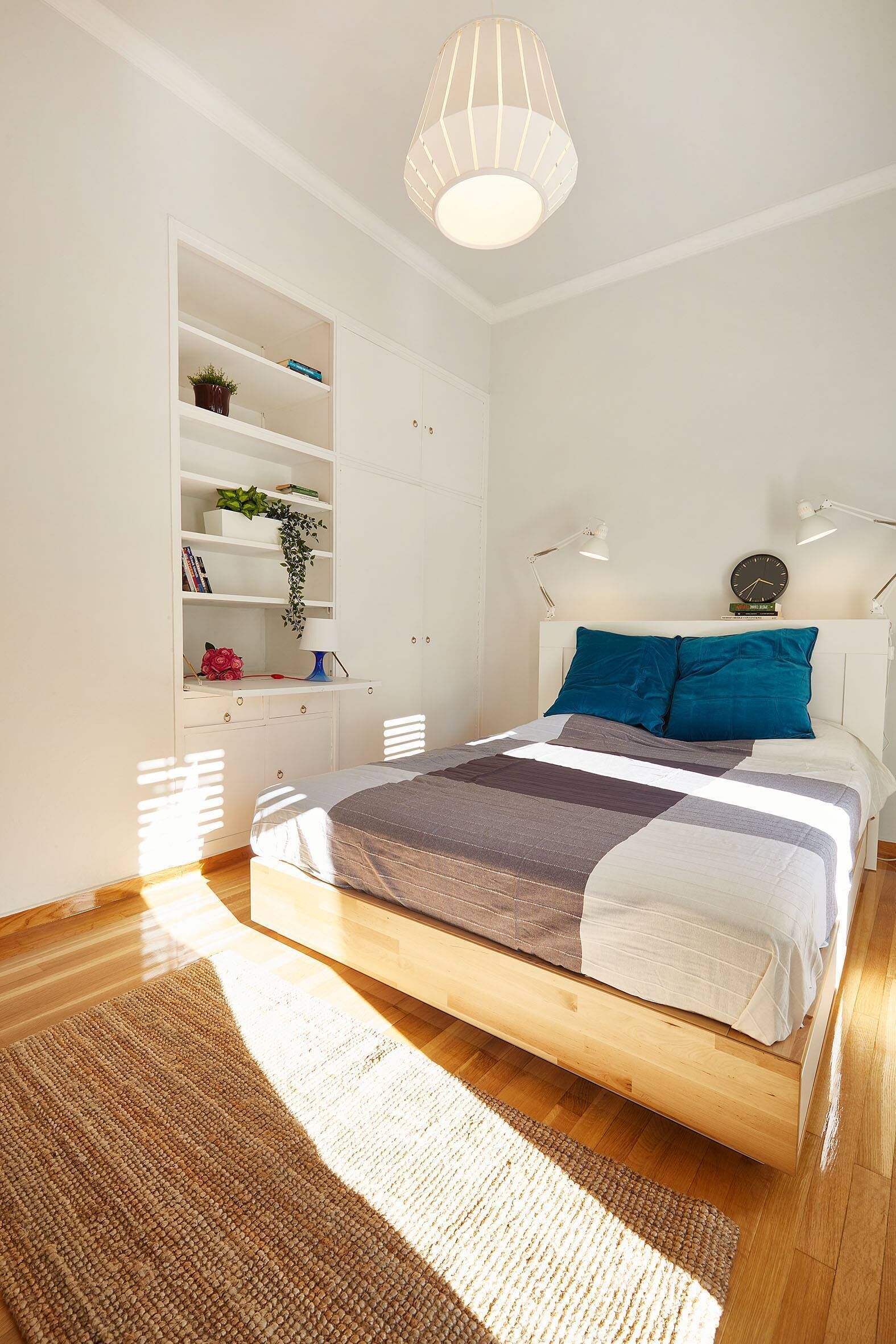 Une chambre à coucher avec un lit, une armoire blanche, une étagère avec des livres et une plante, et une lampe de chevet.
