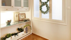 Una habitación con suelo de madera en espiga, muebles blancos con puertas de cristal satinado, una corona decorativa en una ventana y una alfombra estampada.