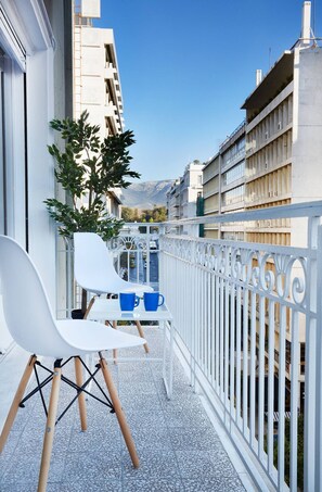 Ein Balkon mit weißen Stühlen, einem Tisch und einem Blumentopf.
