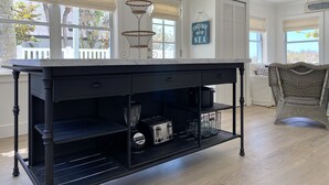 Une cuisine dotée d’un plan de travail en marbre, de meubles de rangement noirs et d’un luminaire suspendu.