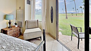 Een hotelkamer met een bed, een stoel, een klein tafeltje met een lamp, een raam met gordijnen en uitzicht op een golfbaan.