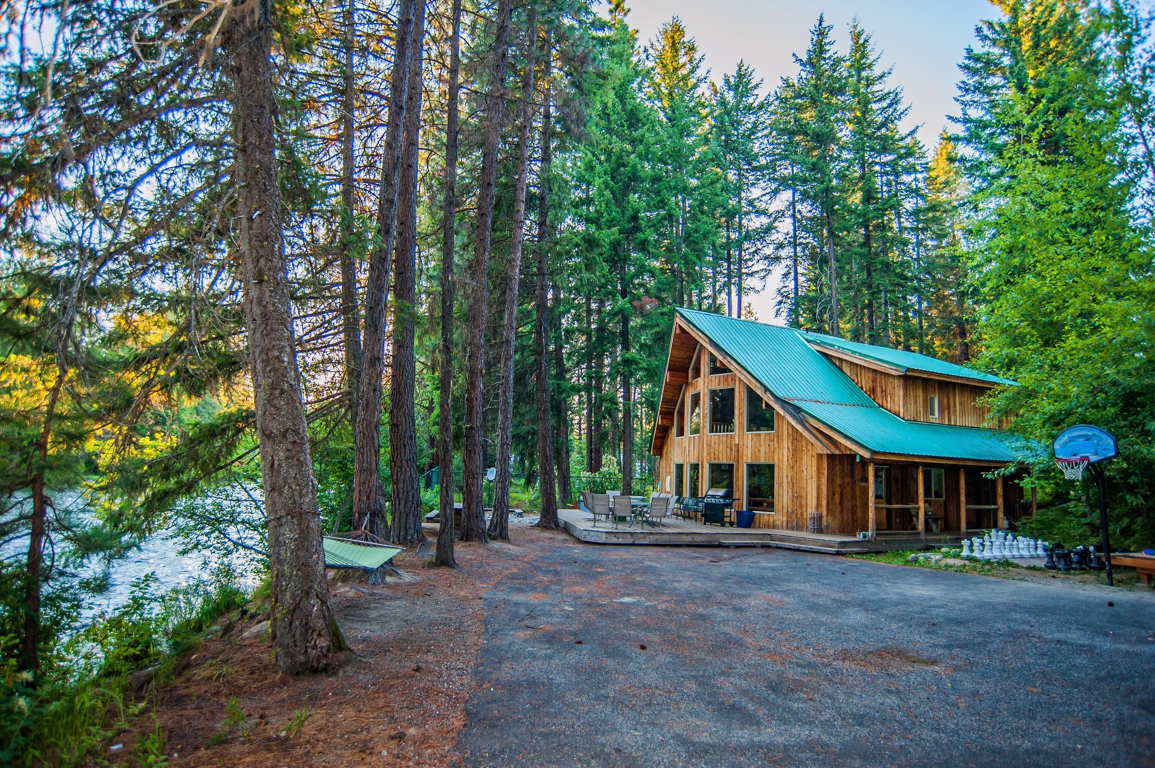 Une cabane dotée d’un toit végétalisé, entourée de grands arbres et bordée d’une allée en gravier.