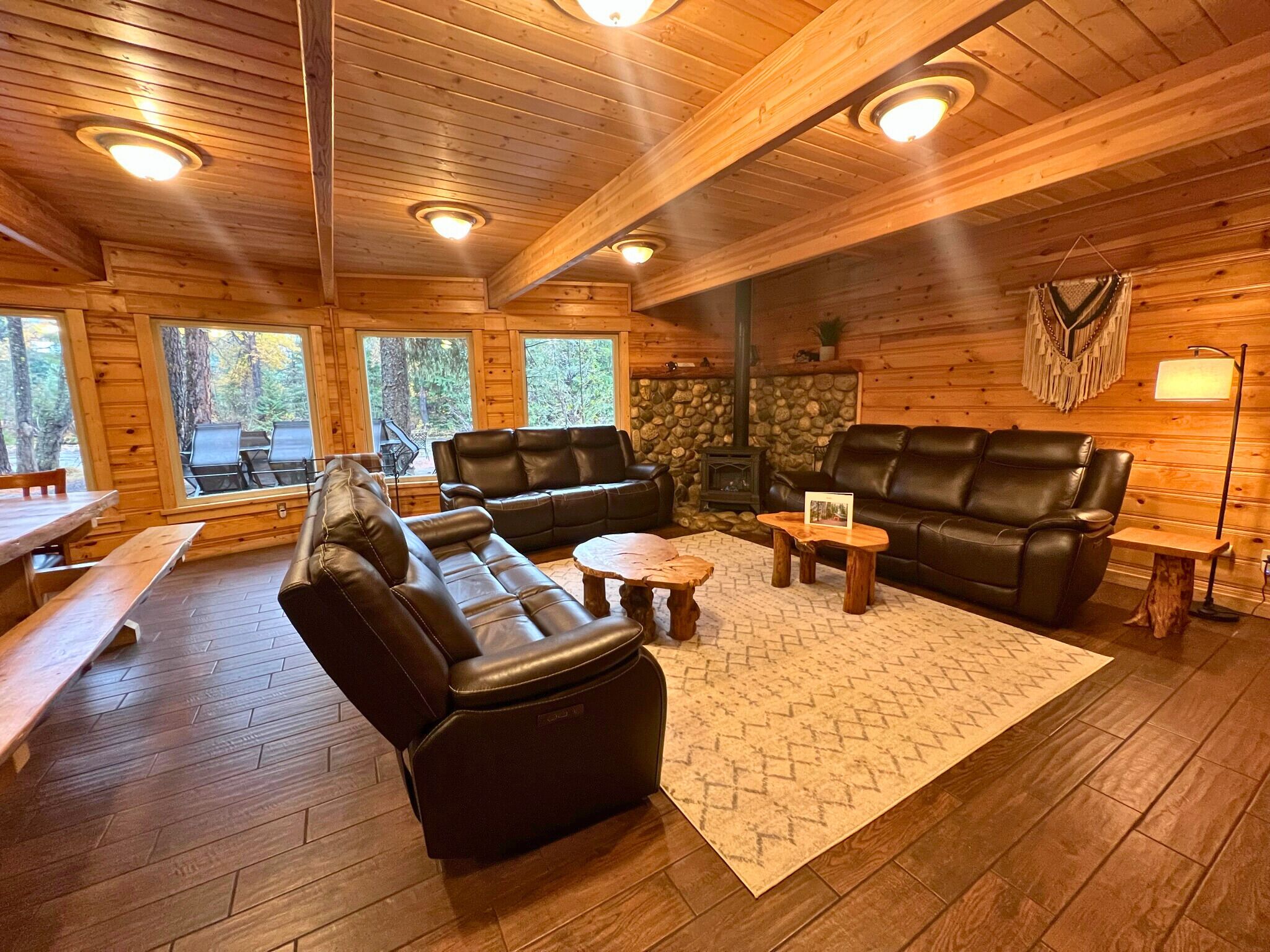 L’intérieur chaleureux d’un chalet avec des murs en bois, une cheminée en pierre, des canapés en cuir et un coin repas avec des bancs.