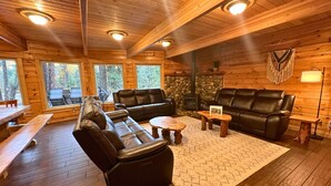 A cozy cabin interior with wooden walls, a stone fireplace, leather sofas, and a dining area with benches.
