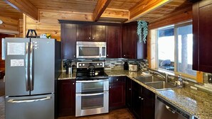 A modern kitchen with wooden ceiling beams, stainless steel appliances, and a granite countertop.
