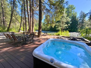A hot tub on a wooden deck with a table and chairs, surrounded by trees and a view of a lake. - Riverfront home, 4 bedrooms! (Leavenworth)