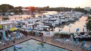A marina with boats docked, a swimming pool with lounge chairs, and a building with a yellow awning.