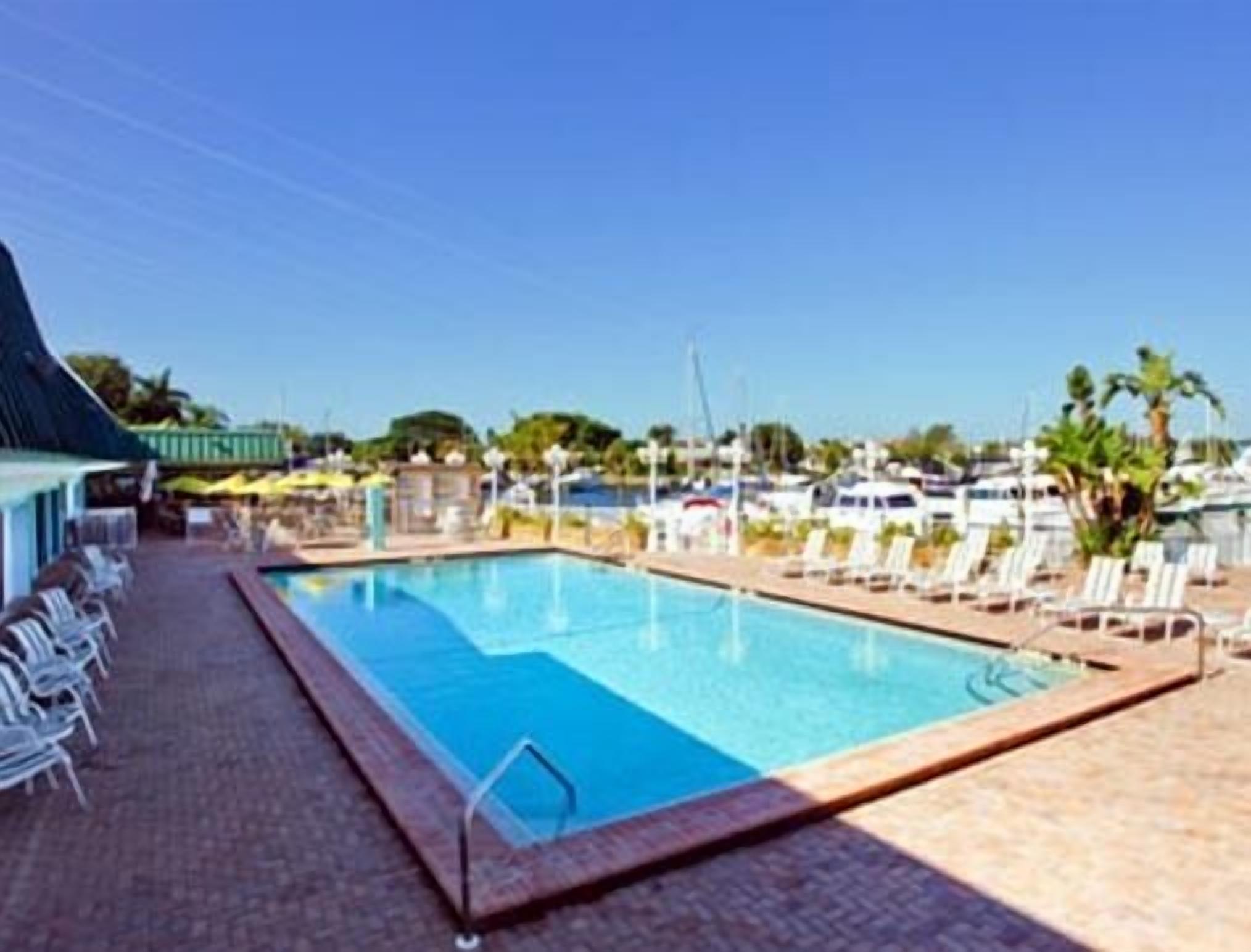 Ein Swimmingpool mit Liegestühlen und einer überdachten Liegefläche, umgeben von Booten und Palmen.