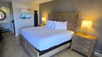 A neatly made bed with a wooden frame and white bedding, flanked by two bedside tables with lamps, in a room with tiled flooring and a painting on the wall.