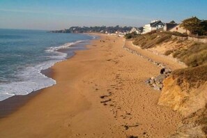 A sandy beach with houses on the right and a clear sky.