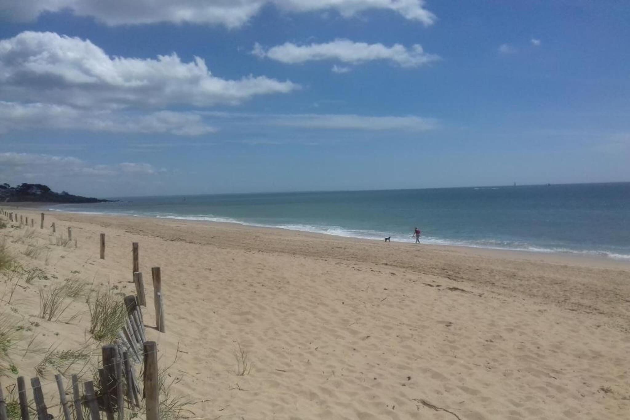 Una playa arenosa con una cerca de madera y una persona caminando por la orilla.