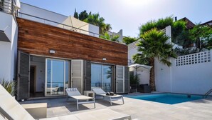 A modern outdoor pool area with two lounge chairs and a wooden wall. - Magnificent Villa with private pool (Almuñécar)