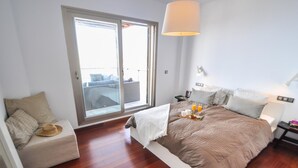 A modern bedroom with a large bed, a small seating area, and a balcony with a view. - Magnificent Villa with private pool (Almuñécar)