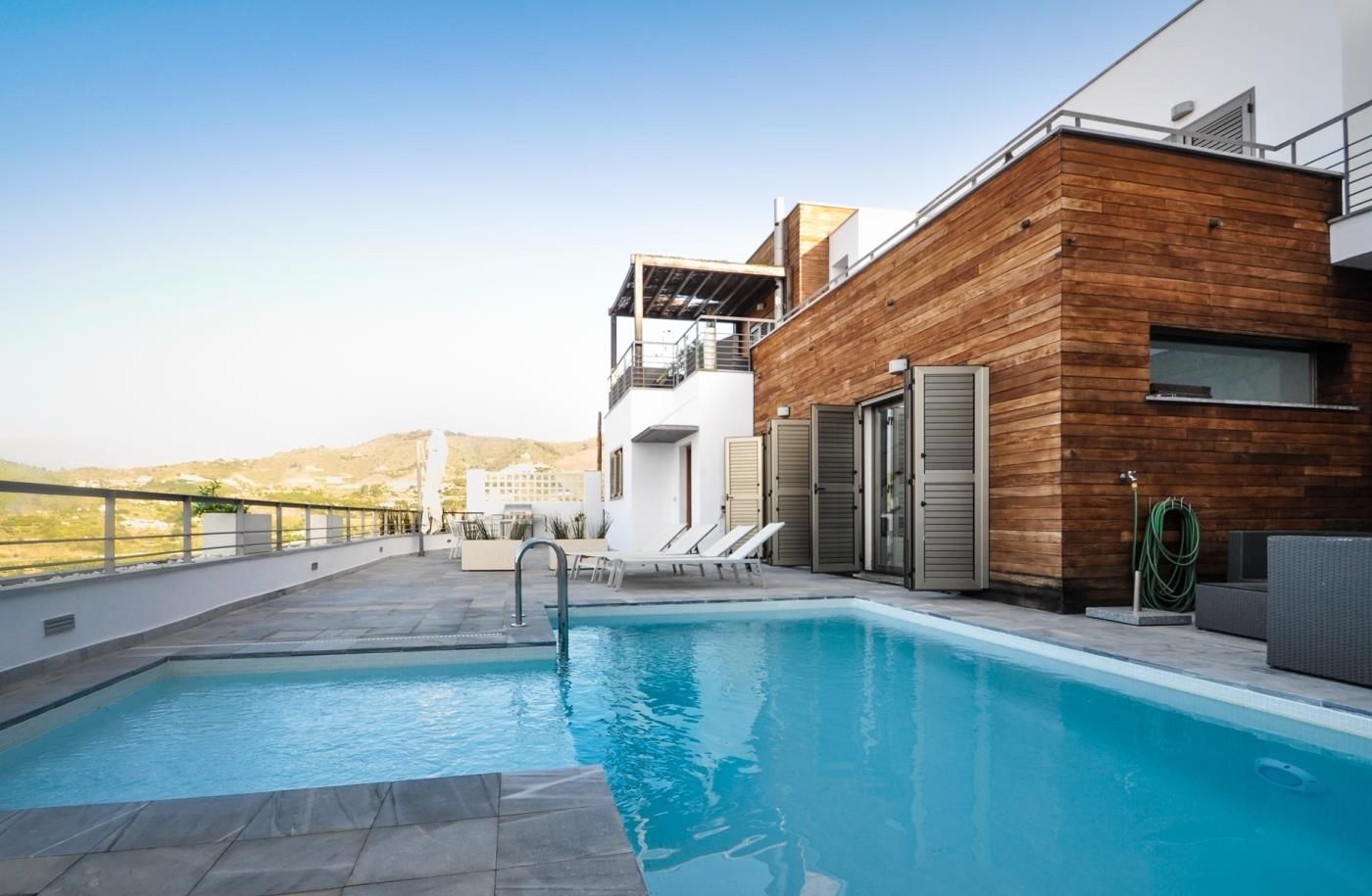 A modern pool area with a wooden exterior wall, a clear blue pool, and a view of the surrounding landscape.