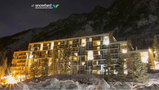 Ein mehrstöckiges Hotel mit moderner Architektur, das Balkone und große Fenster bietet, gelegen in einer gebirgigen, schneebedeckten Landschaft.
