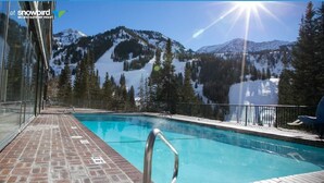 Ein Poolbereich mit Blick auf schneebedeckte Berge, einer Glaskonstruktion und einem Ziegelboden.