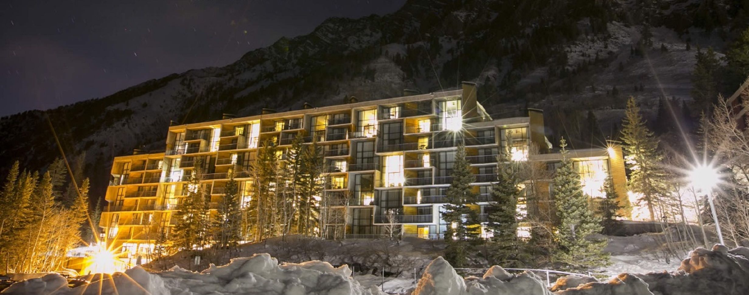 Ein mehrstöckiges Hotel mit moderner Architektur, das Balkone und große Fenster bietet, gelegen in einer gebirgigen, schneebedeckten Landschaft.