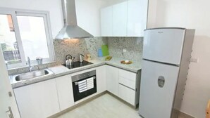 Eine moderne Küche mit weißen Schränken, einer Edelstahl-Dunstesse, einem eingebauten Geschirrspüler und einem Kühlschrank.