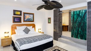 Um quarto moderno com uma cama grande, ventoinha no teto, obras de arte emolduradas e banheiro com chuveiro de vidro.