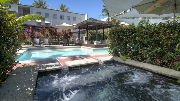 Piscina com hidromassagem, rodeada por guarda-sóis e espreguiçadeiras.
