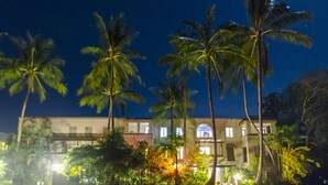 Um edifício com vários andares, varanda e área de jardim com palmeiras.