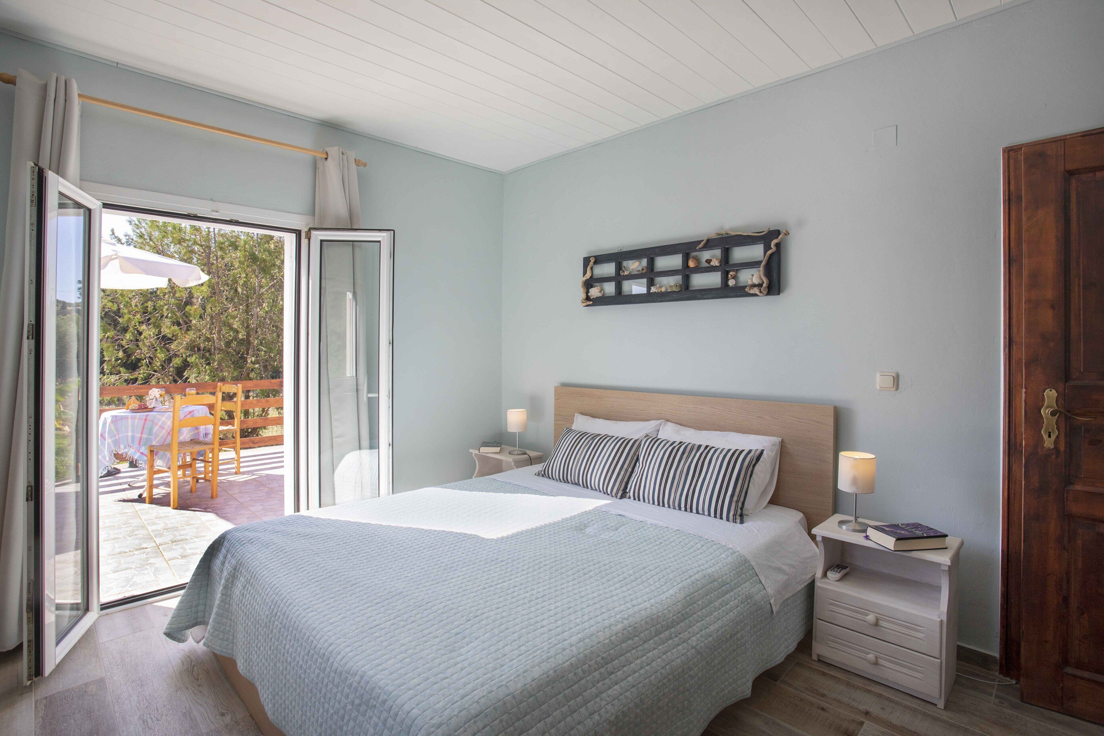 A bedroom with a bed, a nightstand, a wall-mounted shelf, and a sliding glass door leading to an outdoor area.