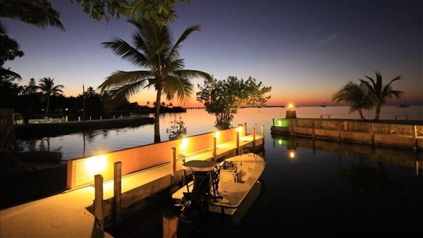 A waterfront area with a dock, palm trees, and a sunset in the background. - Bayside: Bayfront villa W/ free onsite boat ramp marina & trailer parking. (Islamorada)
