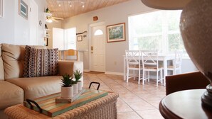 A living room with a beige sofa, a coffee table with a plant, and a dining area with white chairs and a table. - Bayside: Bayfront villa W/ free onsite boat ramp marina & trailer parking. (Islamorada)