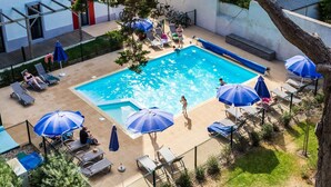 En pool med solstolar och parasoller, omgiven av ett inhägnat område med en byggnad i bakgrunden.