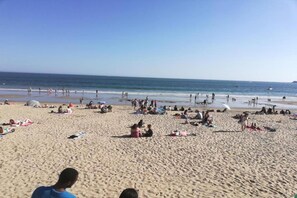 Ein Strand mit badenden und sonnenden Personen, und ein klarer Himmel.
