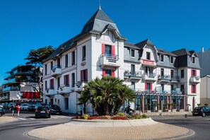 A multi-story hotel with balconies, a central courtyard with palm trees, and a clear blue sky.