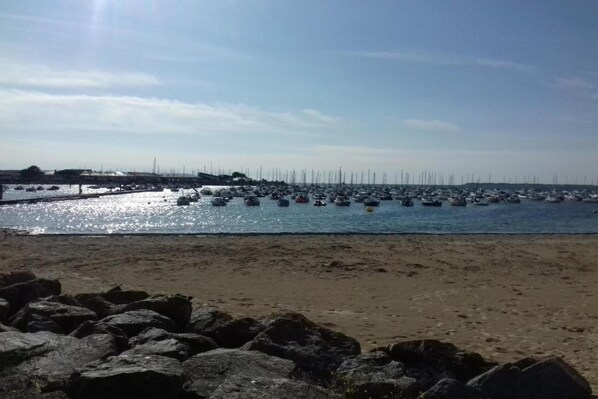 A beach with a rocky foreground and a marina in the background.