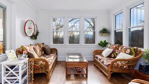 A cozy room with wicker furniture, a glass coffee table, and large windows offering a view of trees. - Afton Station Cottage -Beautifully Renovated Blue Ridge Scenic Historic Setting (Afton)