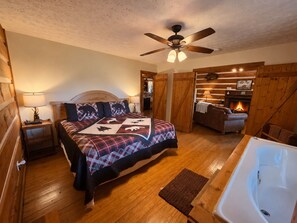 Un dormitorio acogedor con cama, ventilador de techo, chimenea y baño con bañera.
