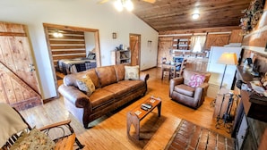 A cozy cabin interior with a wooden ceiling, a leather sofa, a dining table, and a kitchen area. - CJ's Cabin: A Secluded 1-Bedroom Retreat with Mountain Views and Hot Tub (Sieverville)